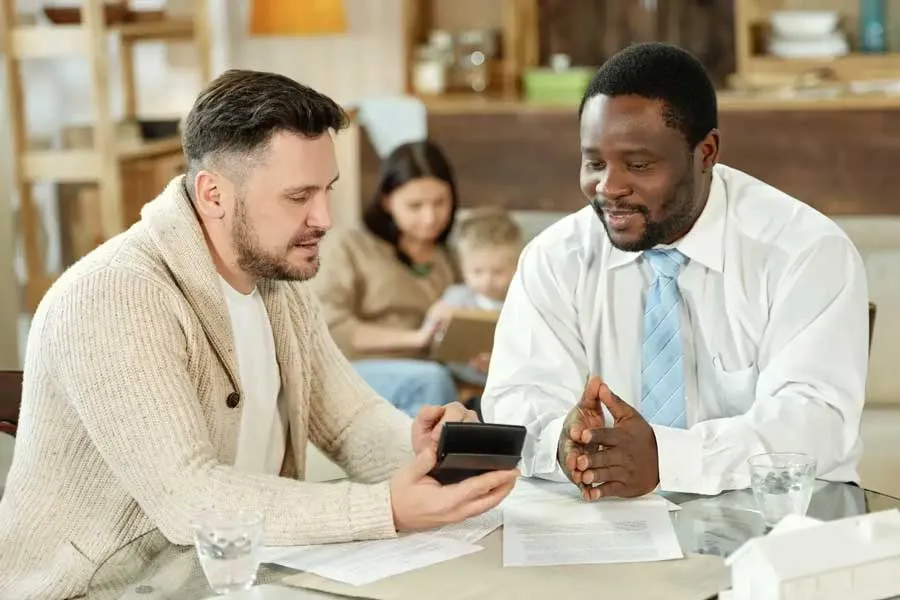 Financial advisor and client review documents and a calculator at a table, exploring options like defence loans for home ownership or investments