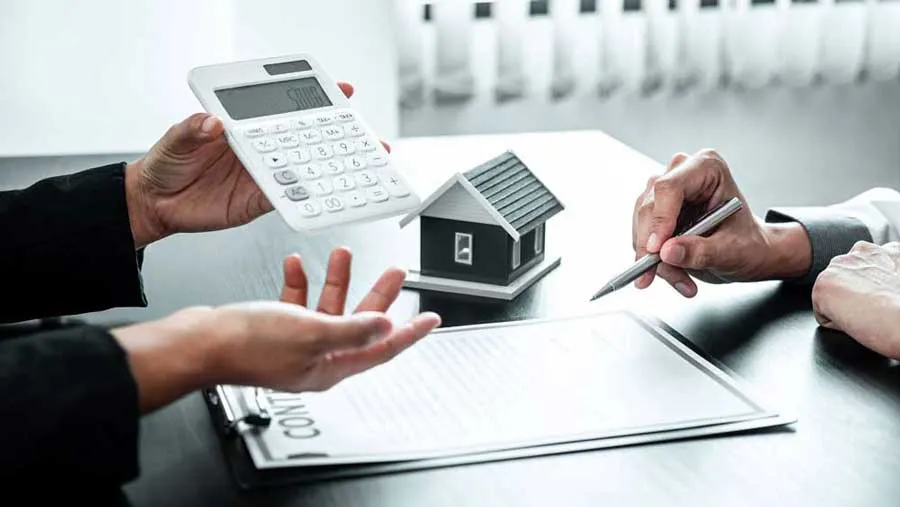 Two individuals negotiating terms over a contract, calculator, and model house, indicating financial planning using defence loans